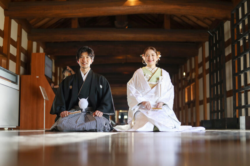 木造建築の廊下で並ぶ新郎新婦の和装フォト・白無垢と黒紋付が落ち着いた和の空間に映える厳かなロケーションショット