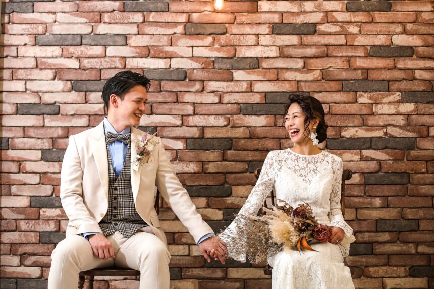 レンガ壁の前で並んで座る新郎新婦のフォトウェディング・ドライフラワーのブーケが映える落ち着いたスタジオショット