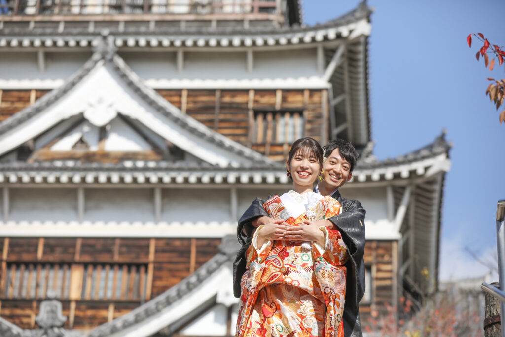 城を背景に並ぶ和装の新郎新婦のフォトウェディング・歴史的建築が映える和のロケーション