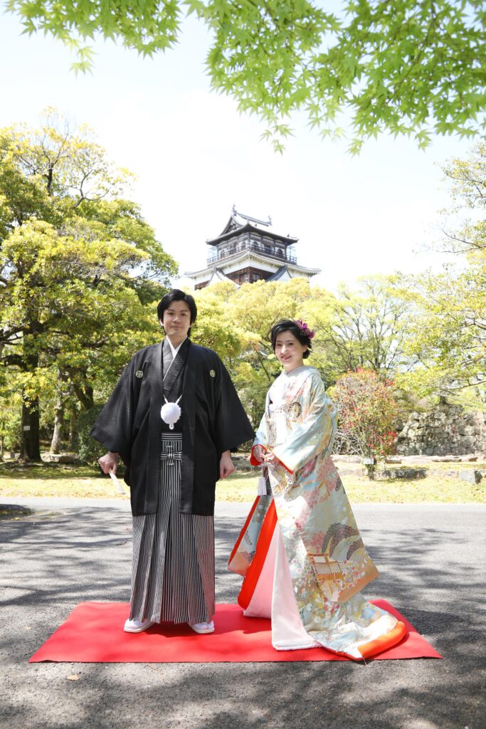 城を背景に番傘を持つ和装の新郎新婦の前撮り・歴史的建造物が映える広島らしいロケーション