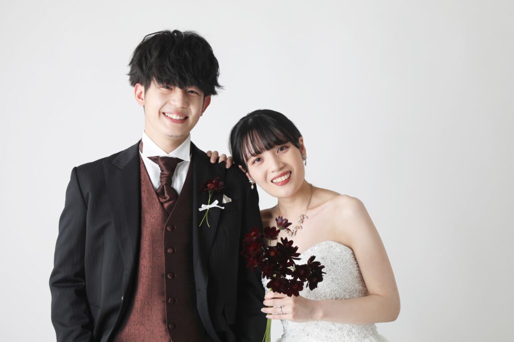 白い背景の前で並ぶ新郎新婦のフォーマルフォト・黒スーツと白ドレスが映えるシンプルで洗練された一枚