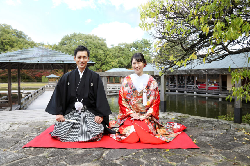 池のほとりで赤い毛氈に座る新郎新婦の和装ロケーションフォト・伝統的な装いが庭園の静けさに溶け込む一枚