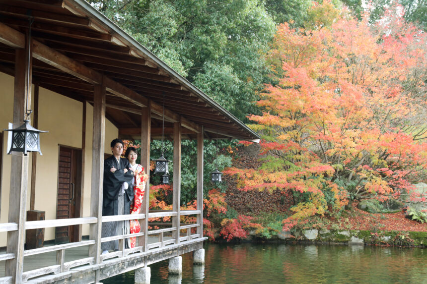 回廊で並ぶ新郎新婦の和装ロケーションフォト・紅葉と池が彩る秋の庭園での穏やかな一枚