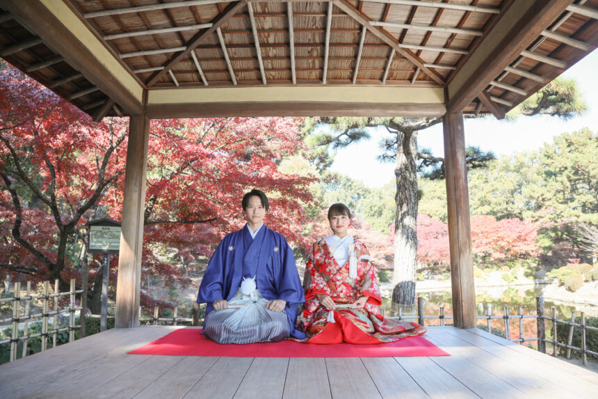 東屋で並んで座る新郎新婦の和装ロケーションフォト・紅葉の庭園を眺める落ち着いた秋の一枚
