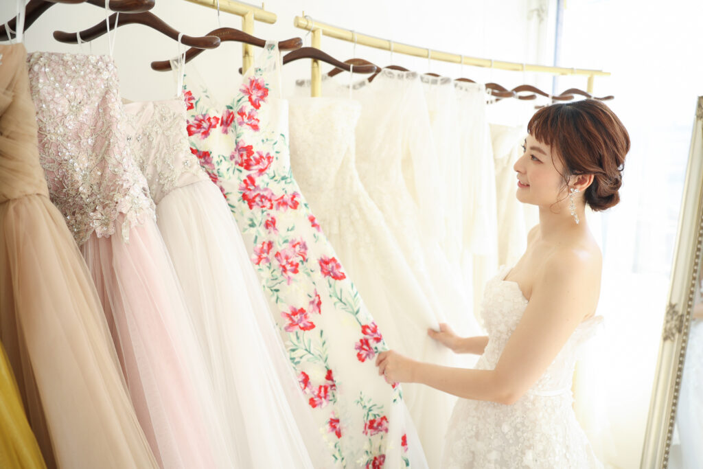 ドレスが並ぶラックの前で衣装を選ぶ花嫁のフォトウェディング・多彩なドレスが並ぶ明るいブティックでの一場面