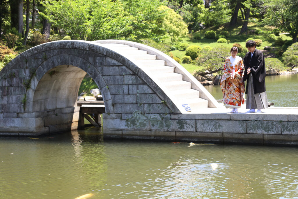 縮景園の石橋で並ぶ和装の新郎新婦のフォトウェディング・庭園の緑が映える城ロケーション