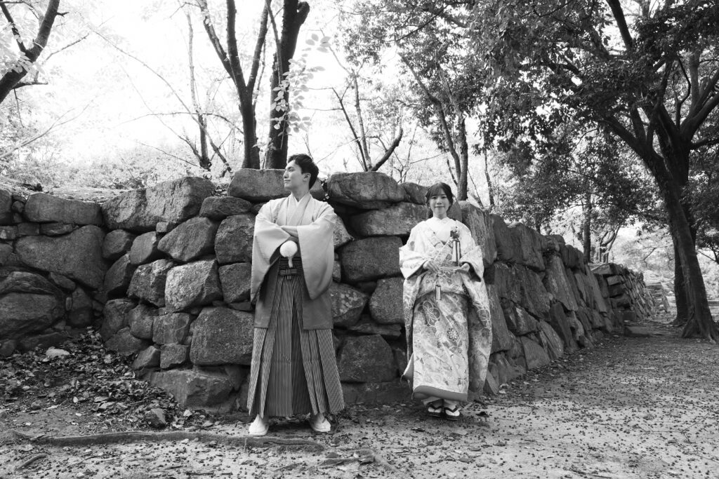 広島城の石垣を背景に佇む和装の新郎新婦のフォトウェディング・歴史を感じるモノクロショット